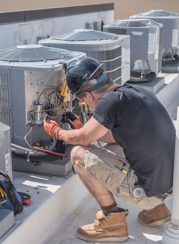 Hvac tech on roof top checking a condenser unit, with condensers in the background.